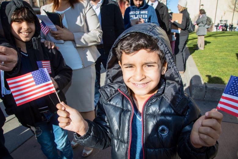 Zain, 6, waves two American flags. When his parents take the oath of citizenship, he and his brother also become U.S. citizens.