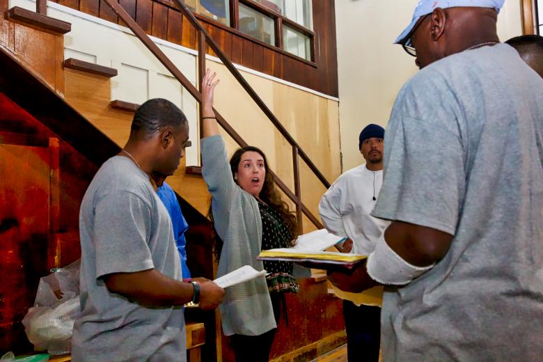 Alejandra Wahl, development associate for the Marin Shakespeare Company, directs inmates during a song rehearsal for “The Tempest” at Folsom State Prison. (Photo by Steve Martarano)