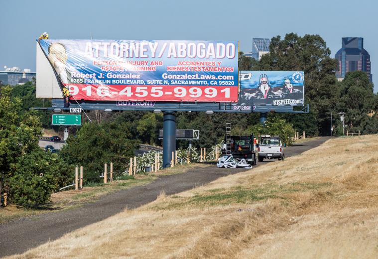On this morning, the men first pull down an old vinyl (billboard speak for “sign”) before installing the new one — advertising a local law firm — as commuters speed past on the road below. On this morning, the men first pull down an old vinyl (billboard speak for “sign”) before installing the new one — advertising a local law firm — as commuters speed past on the road below.