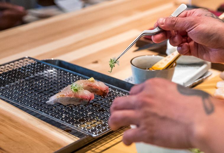 Ngo finishes a piece of yellow jack (or shima aji) nigiri with grated ginger and green onion; on the left, he uses a butane torch to finish a sea urchin nigiri with toasted seaweed. “Try to eat nigiri in one bite — if it’s dressed already, it’s meant to be a perfect bite,” Ngo advises.