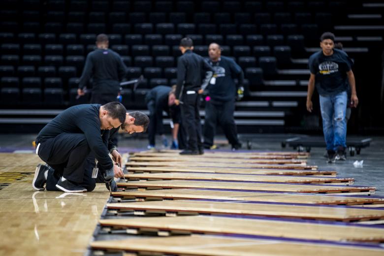 Four individuals place each panel, and a fifth member locks it in place with a steel pin as another group approaches from behind with the next panel.