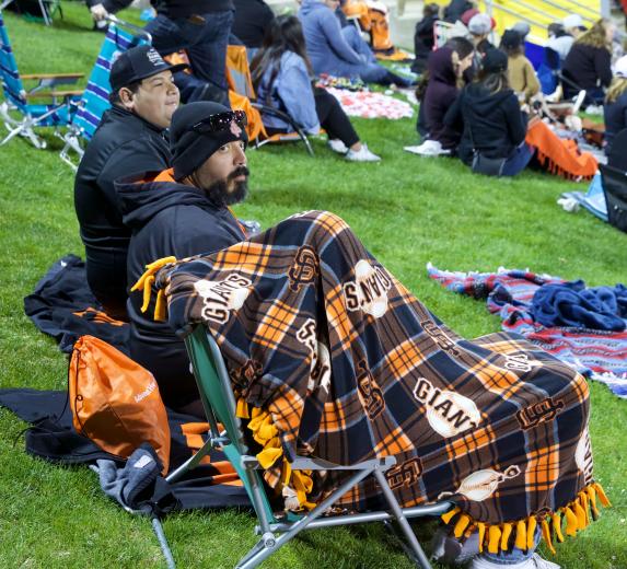 Omar Balderas, Matthew Sanchez and Kadence Sanchez (covered) try to stay warm from their perch beyond the right field foul pole at Raley Field Saturday night.