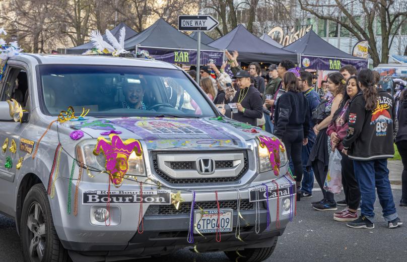 A vehicle festooned with Mardi Gras decorations cruises by the event's bar tents.