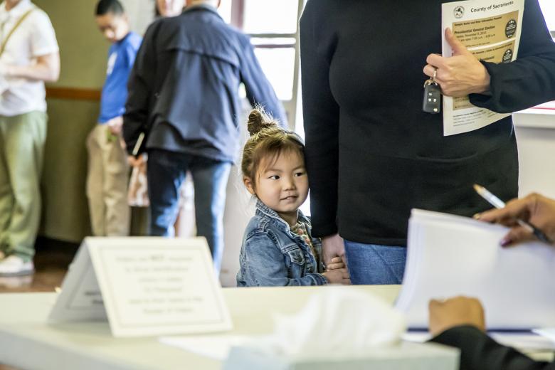Four-year-old Elliott Webb hides behind her mother, Toni Webb, who checks in to obtain her ballot.