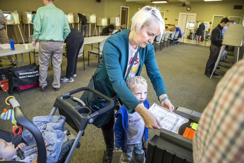 Samson Kelahan helps his mother, Kristen Schumacher, scan her completed ballot, as baby Lincoln watches from his stroller.