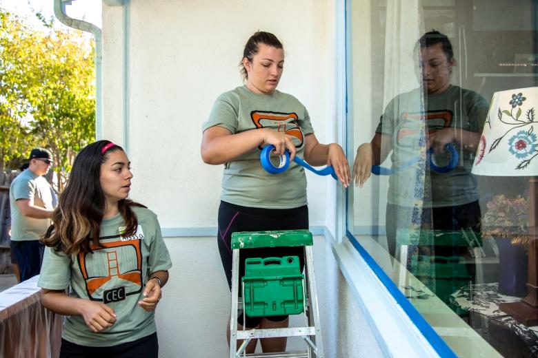 Sac State students Alyssa Carrillo (left) and Sarah Pereira tape the front window of the home on Orinda Way to prepare for painting. Sac State students Alyssa Carrillo (left) and Sarah Pereira tape the front window of the home on Orinda Way to prepare for painting.