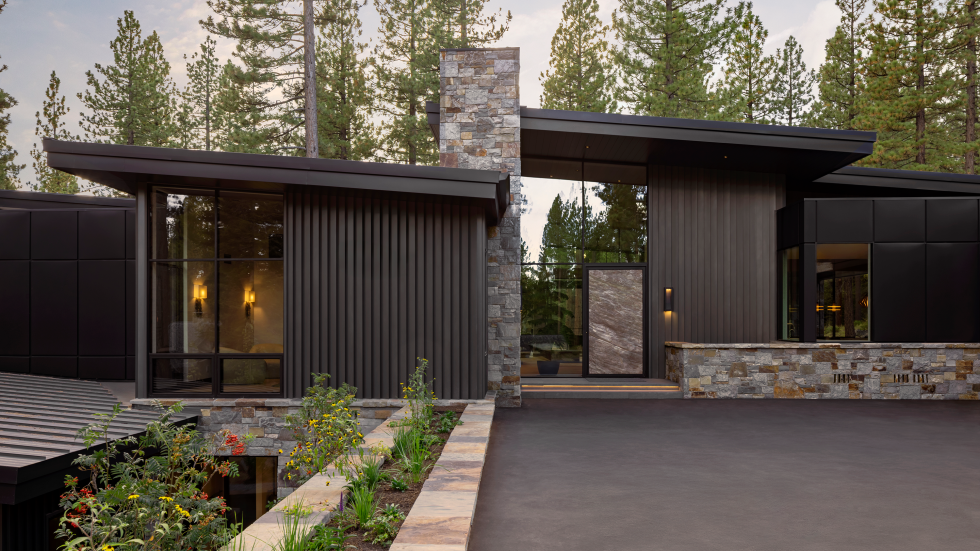 From the rear, the home reveals its full vertical drama with steel-framed expanses of glass extending toward forested views and anchored by Montana ledge stone and corrugated metal. (Photo by Stephanie Russo)